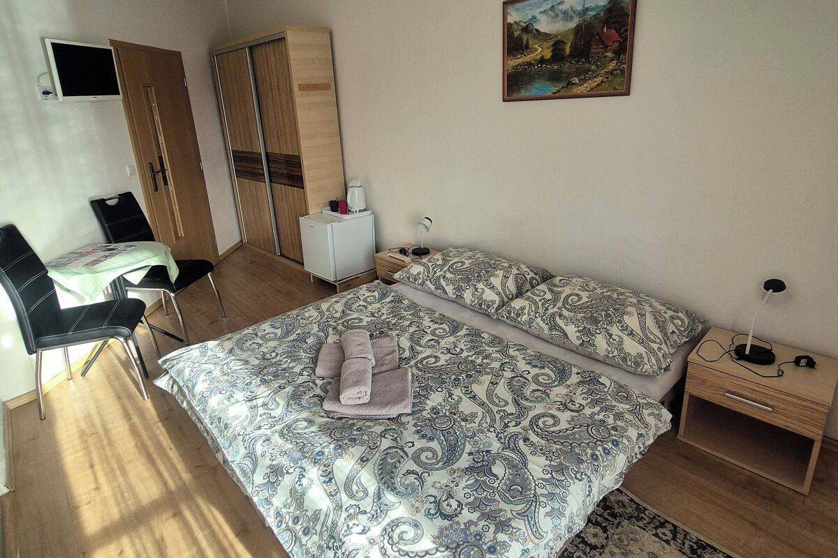 Un dormitorio con cama, escritorio, silla, armario, un cuadro y mesita de noche.