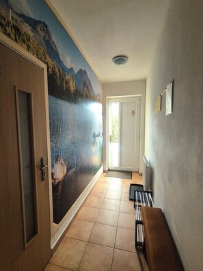 Un pasillo con un mural de paisaje montañoso, una puerta con manija, un radiador y un banco.