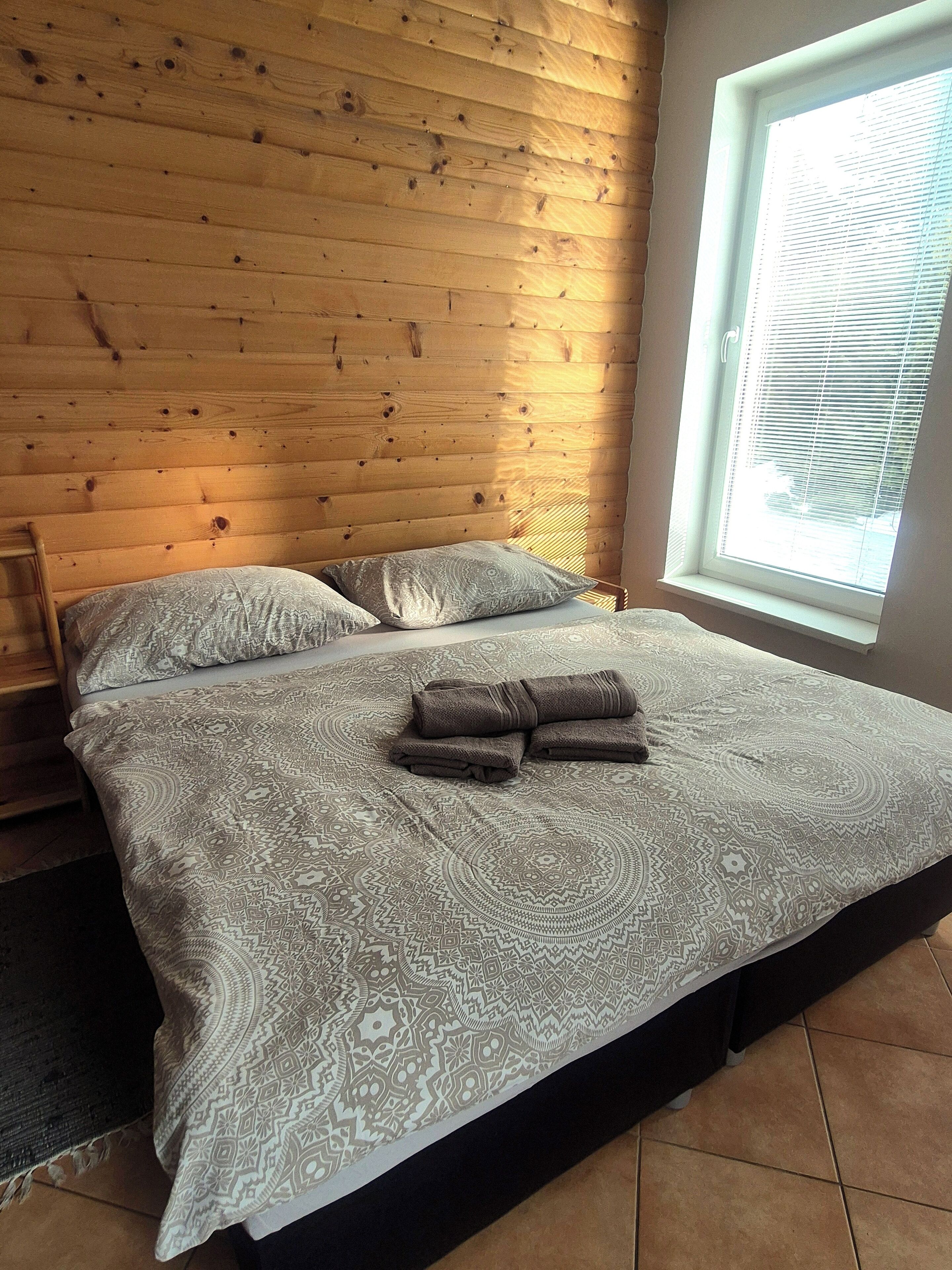 Una cama con ropa de cama estampada, una ventana con persianas y paneles de madera en la pared.