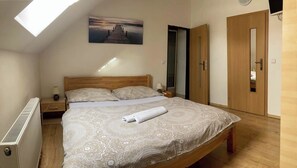 A bedroom with a skylight, a bed with patterned bedding, a bedside table with a lamp, and a wooden wardrobe.