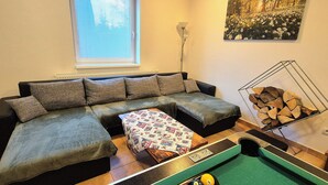 Ett vardagsrum med en hörnsoffa, ett biljardbord och en tavla på väggen.