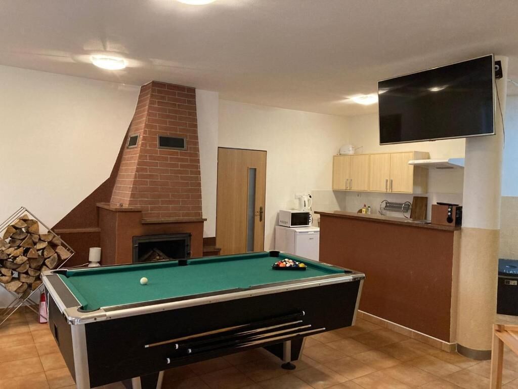 Una mesa de billar en una habitación con chimenea, un área de cocina y un televisor montado en la pared.