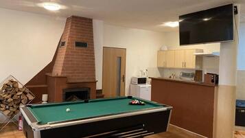 Una mesa de billar en una habitación con chimenea, un área de cocina y un televisor montado en la pared.