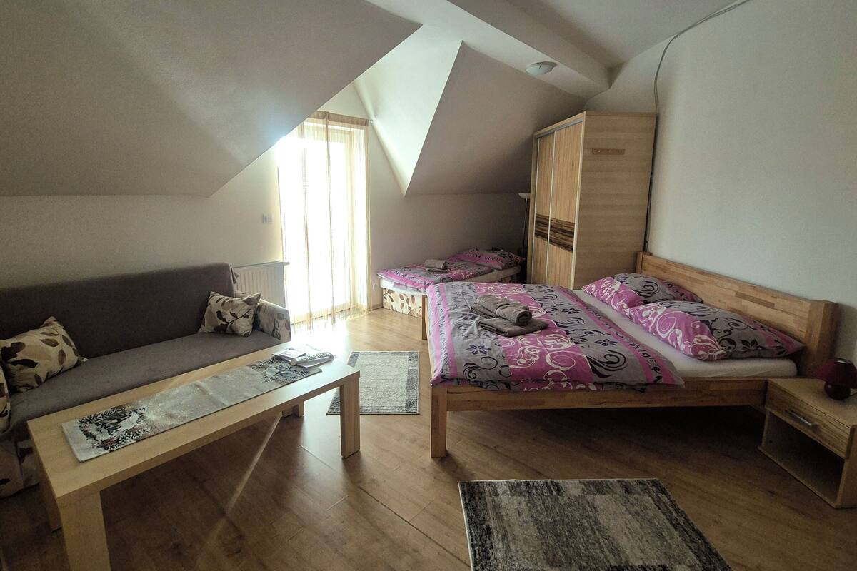 Un dormitorio estilo loft con techo inclinado, un sofá, dos camas con ropa de cama estampada, un armario de madera y una mesita.