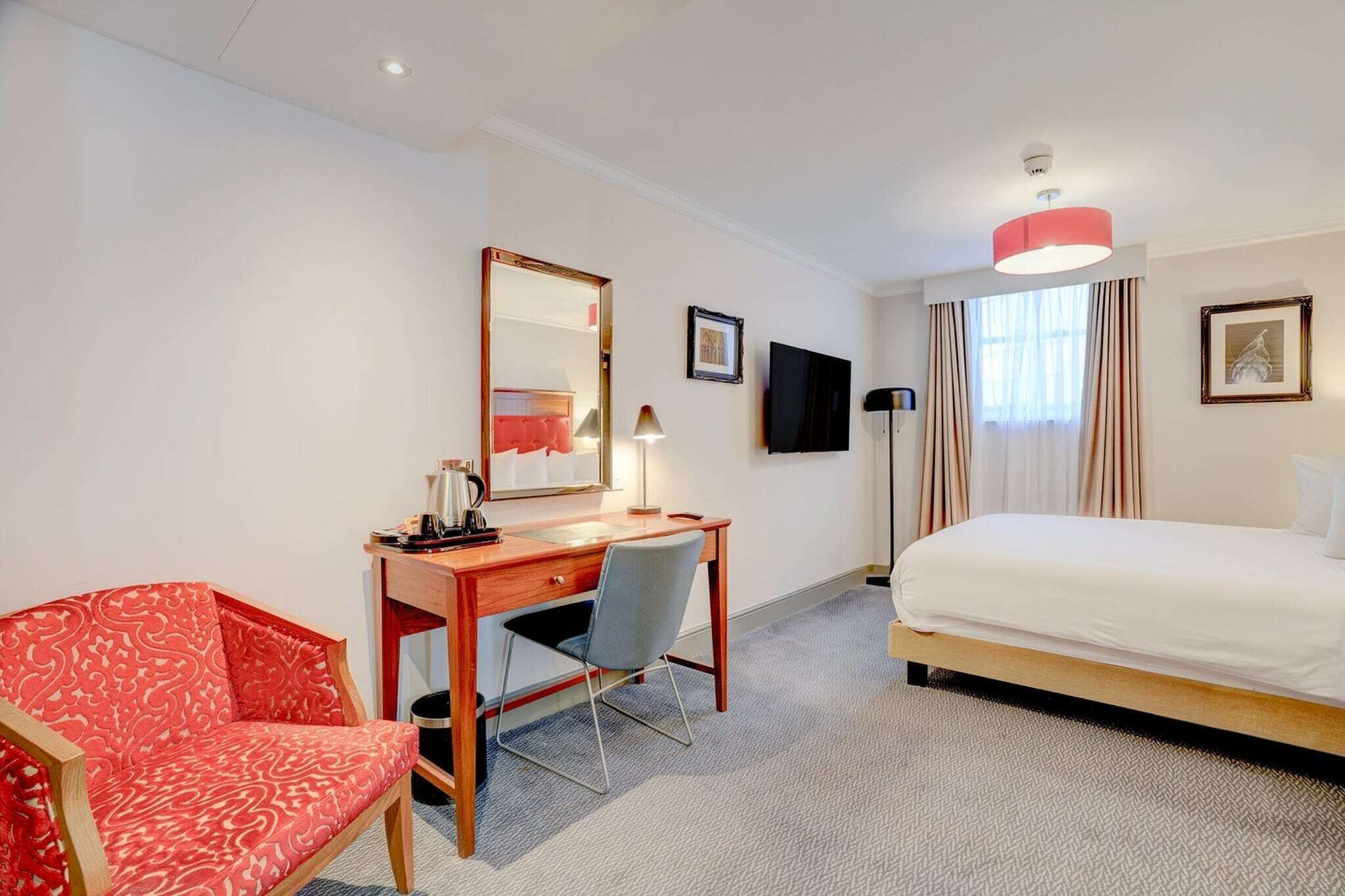 A hotel room with a bed, desk, chair, and a large mirror.