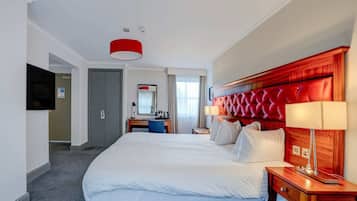 A hotel room with a large bed, a desk, a chair, a television, and a red accent wall.