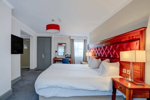 A hotel room with a large bed, a desk, a chair, a television, and a red accent wall.