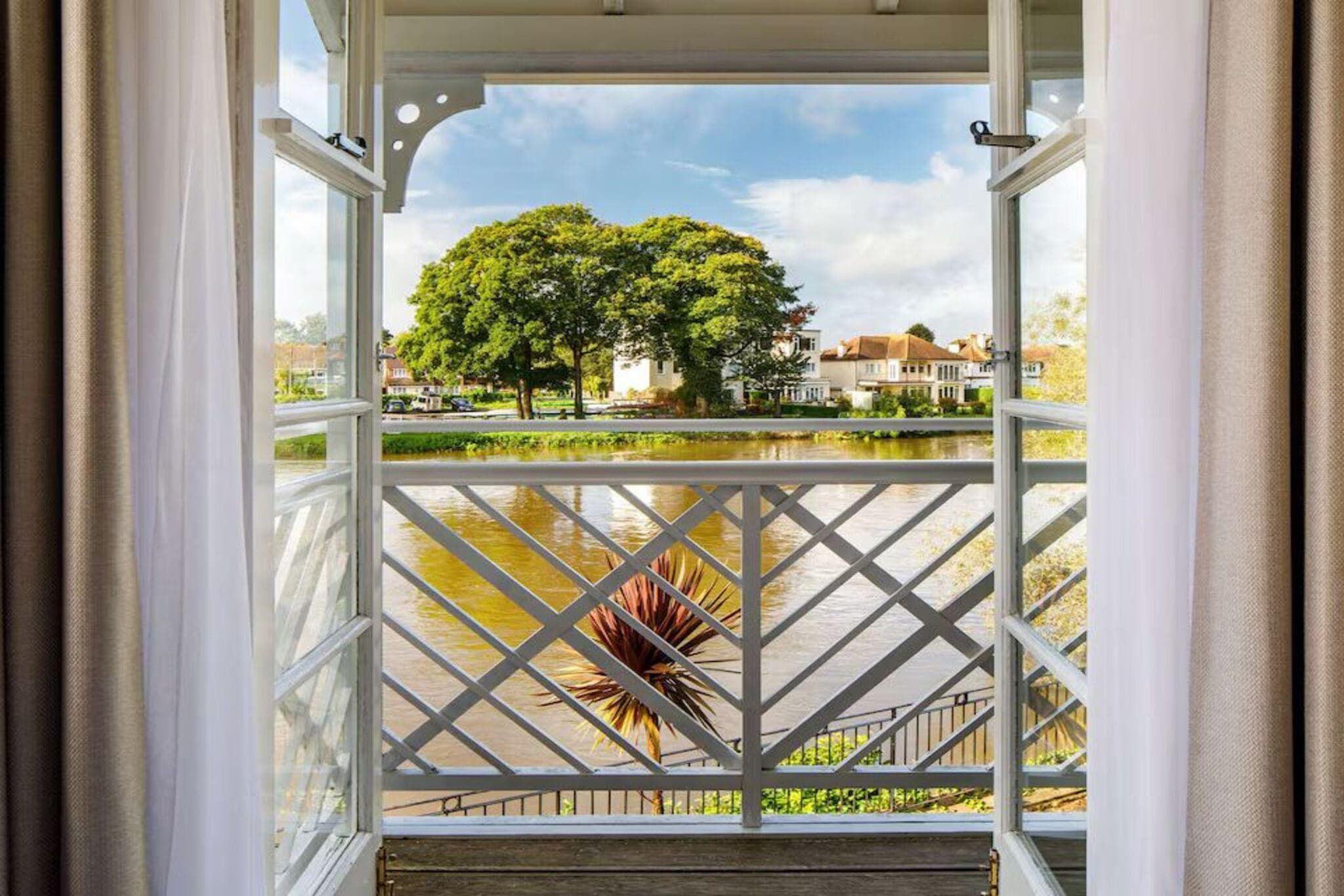 A view from a balcony with a metal railing, overlooking a body of water and a park with trees.