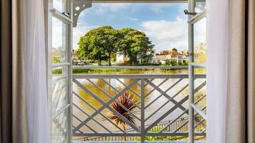 A view from a balcony with a metal railing, overlooking a body of water and a park with trees.