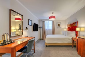 Una habitación de hotel con cama, escritorio, silla y un espejo grande.