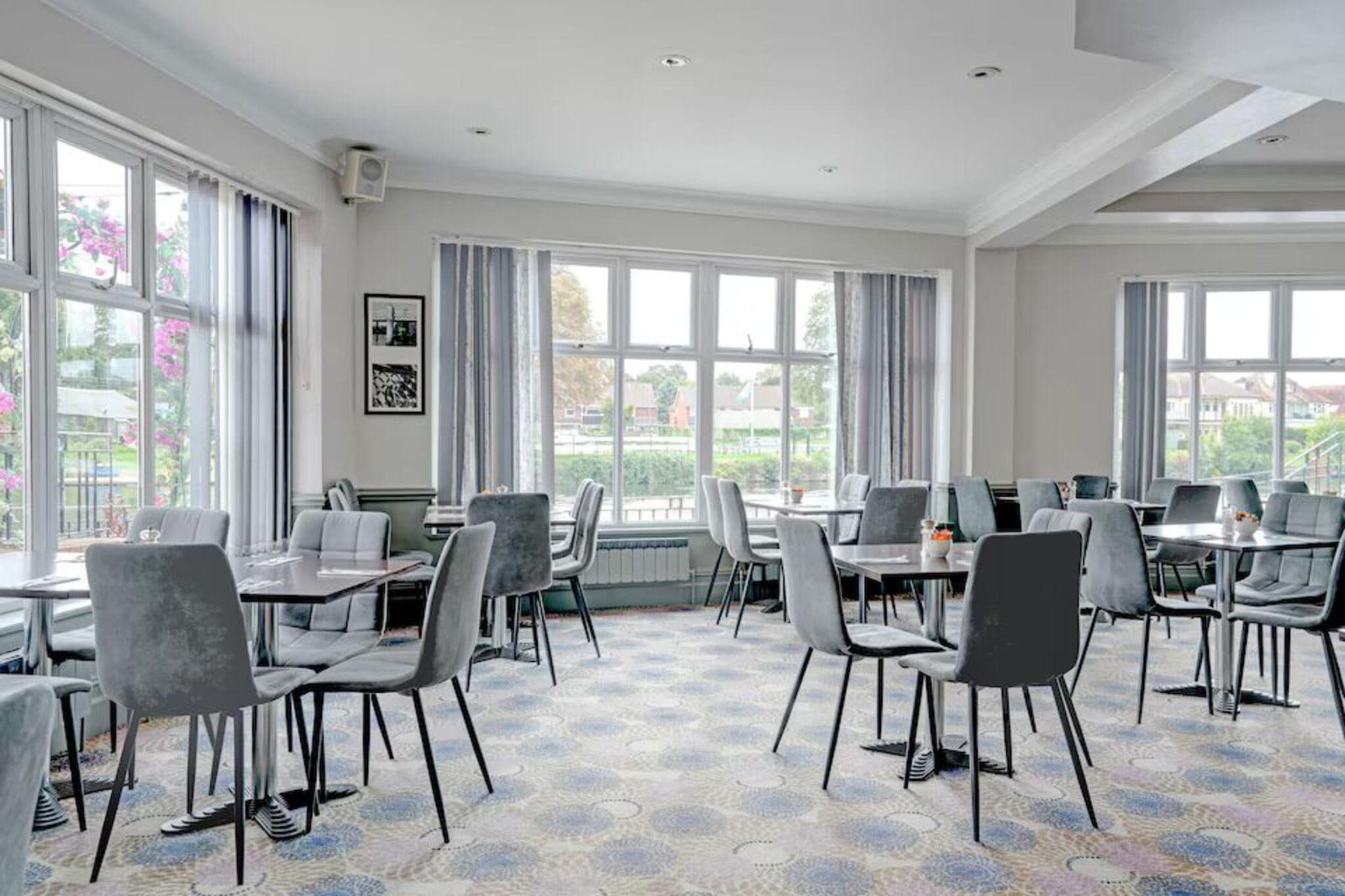 A conference room with multiple tables and chairs, large windows with curtains, and a patterned carpet.