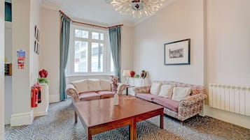 A room with a sofa set, a wooden coffee table, a patterned carpet, a window with curtains, and a wall-mounted picture.