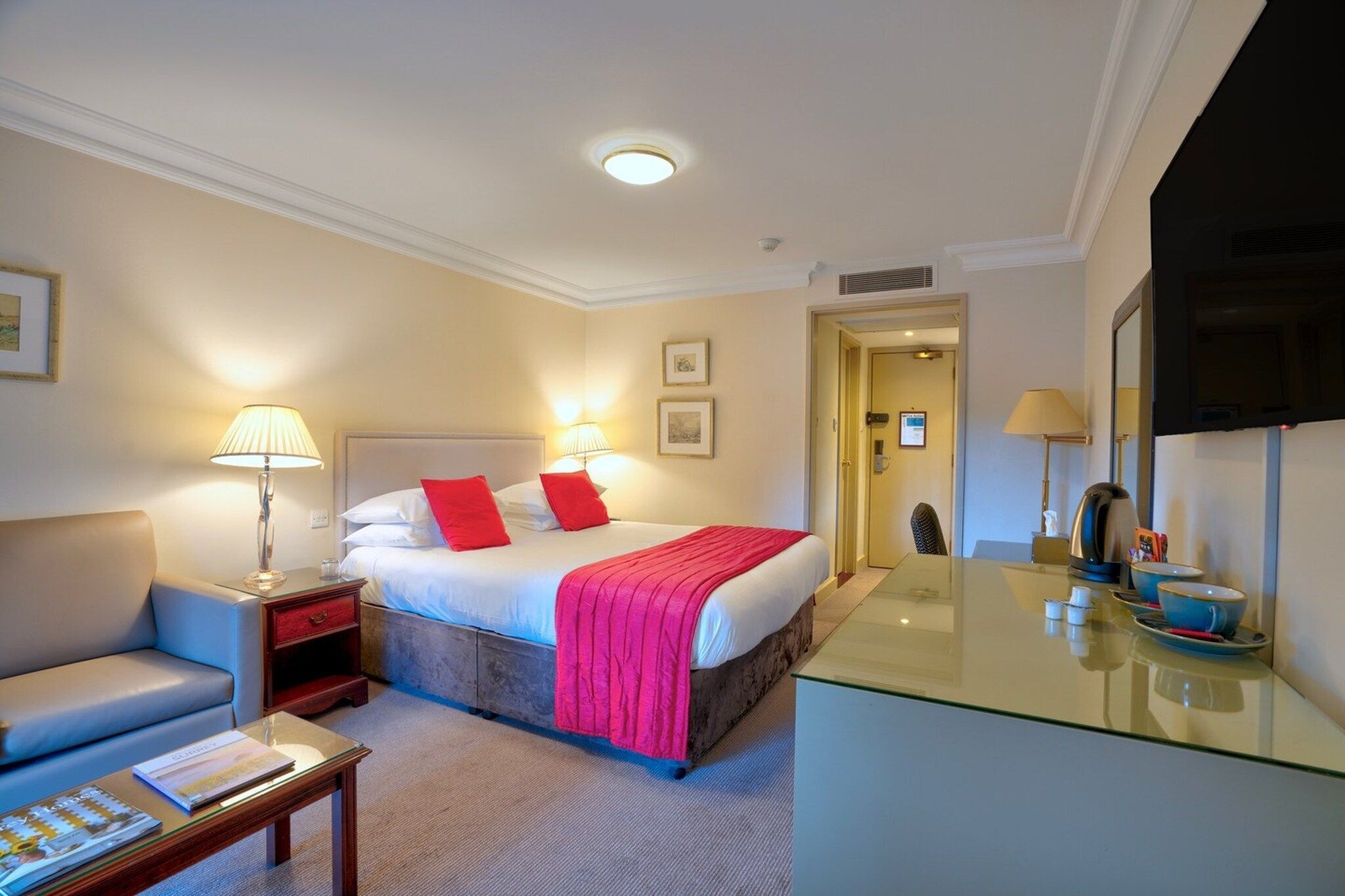 A hotel room with a bed, bedside tables, a sofa, a desk, and a television.