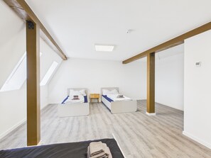 Une chambre avec deux lits, une lucarne et une poutre en bois au plafond.