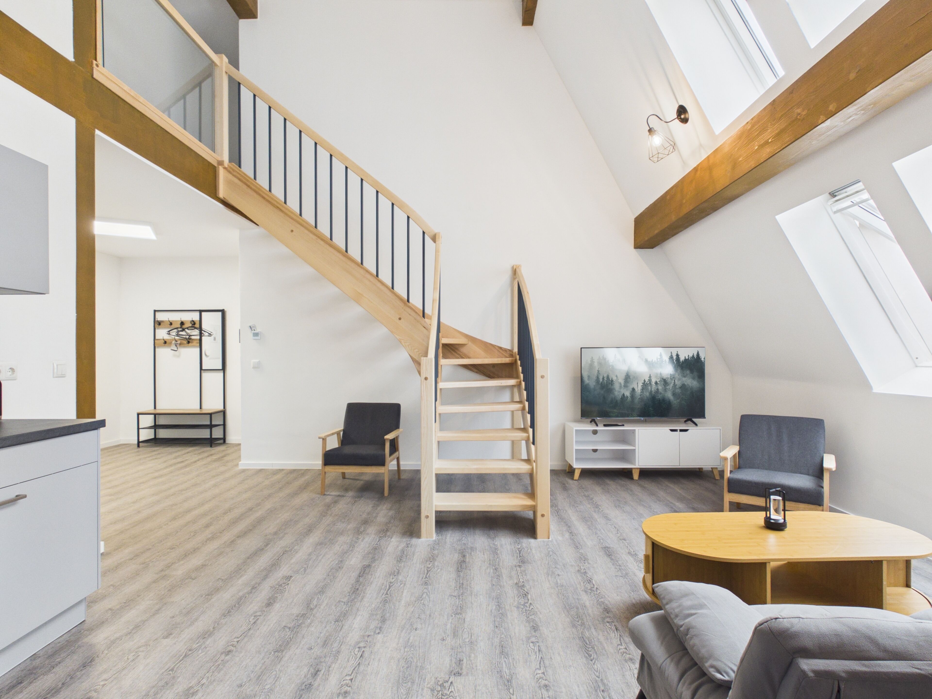 A spacious loft with a wooden staircase, a TV, and a cozy seating area.