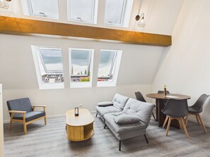 Un intérieur moderne avec un plafond de style industriel, un canapé gris, une table basse ronde en bois et une table à manger avec des chaises.