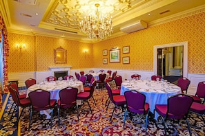 A banquet hall with round tables, red chairs, a chandelier, and patterned wallpaper. - Standard Single Room (Exeter)