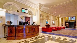 En hotellobby med en receptionsdisk, en klocka, en tv och en trappa.