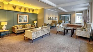 A spacious living room with a patterned carpet, a sofa, armchairs, a coffee table, and a fireplace. - Superior Double Room (London)