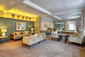 A spacious living room with a patterned carpet, a sofa, armchairs, a coffee table, and a fireplace.