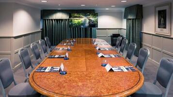 A conference room with a long table, chairs, a television screen, and a framed picture on the wall.