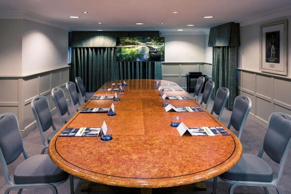 A conference room with a long table, chairs, a television screen, and a framed picture on the wall.