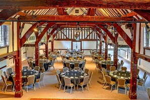 Un vaste hall dotĂ© de nombreuses tables et chaises rondes, de poutres en bois et de grandes fenĂȘtres.
