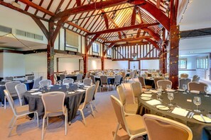 A conference room with multiple tables and chairs, wooden beams, and a high ceiling.