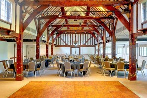 A large hall with high wooden beams, multiple tables set for dining, and a carpeted floor.