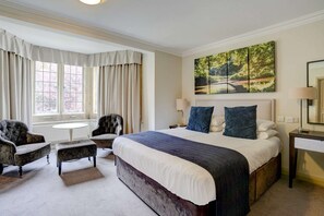 Una habitación de hotel con una cama grande, dos sillones, una mesita redonda y un cuadro en la pared.