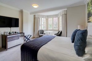 A hotel room with a bed, a desk, a chair, a TV, and a window with curtains.
