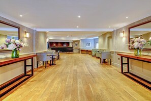 A spacious hotel lobby with a wooden floor, a reception desk, seating area, and a bar.