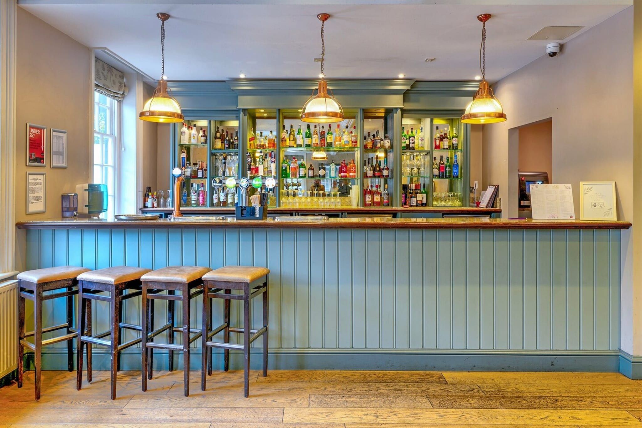 A bar area with stools, a counter with bottles, and hanging lights.