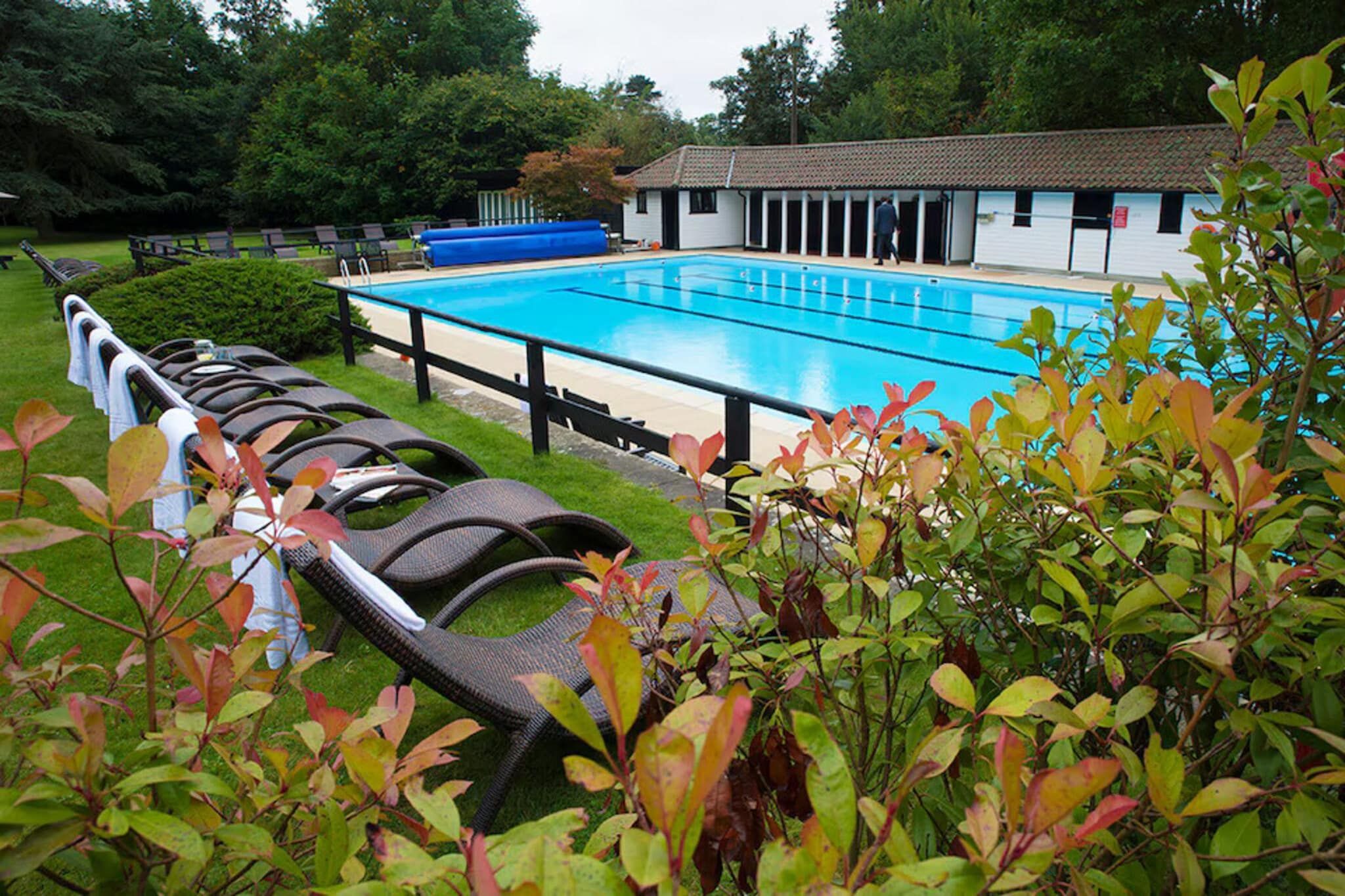 Une piscine avec des chaises longues, un espace de détente couvert et un bâtiment doté d’un toit en tuiles.
