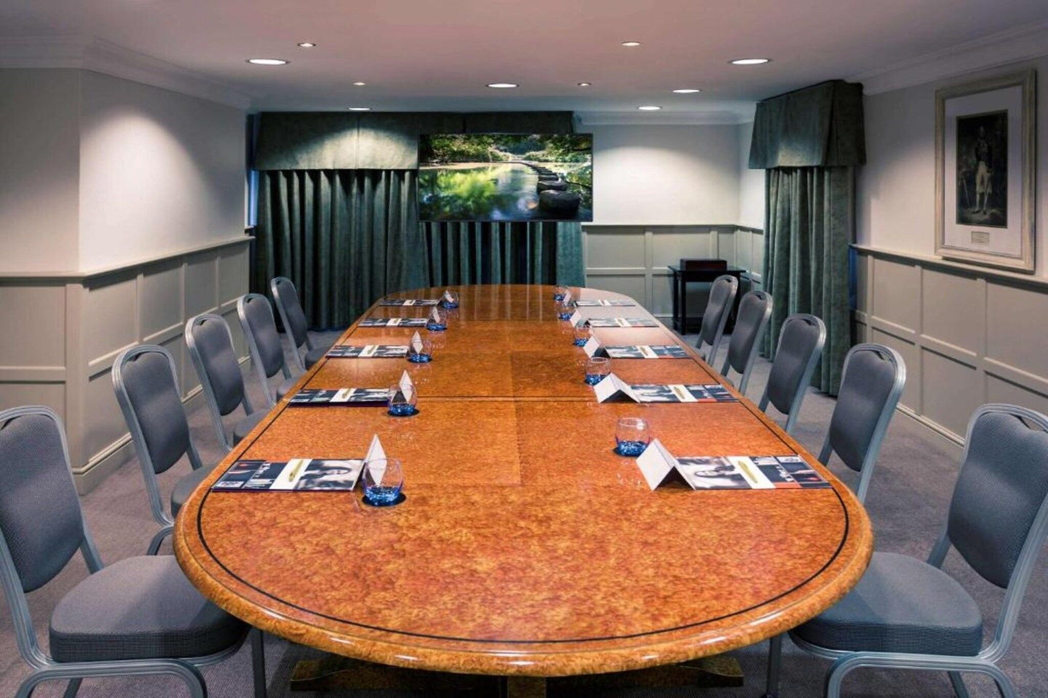 A conference room with a long table, chairs, name cards, and a scenic wall mural.