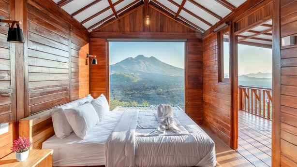 Ein Schlafzimmer einer Holzhütte mit Bett, einem kleinen Nachttisch, einer Topfpflanze und Bergblick.