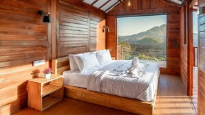 Ein Schlafzimmer in einer Holzhütte mit Bett, Nachttisch und Blick auf eine Berglandschaft.