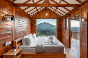 A wooden cabin with a bed, a bench, a potted plant, and a view of a mountain. - Kamani Cabin (Bali)