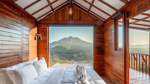 Ein Holzhüttenraum mit einem Bett, Blick auf einen Berg und einem Balkon.