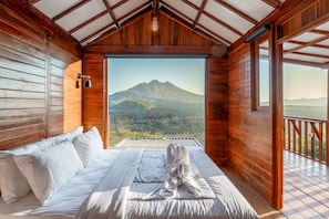 Ein Holzhüttenraum mit einem Bett, Blick auf einen Berg und einem Balkon.