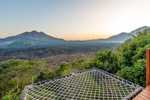 A hammock with a netted cover, surrounded by greenery and a mountainous landscape. - Kamani Cabin (Bali)