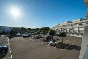Ein Parkplatz mit mehreren Autos, ein Gebäude mit Balkonen und einem wolkenlosen Himmel.