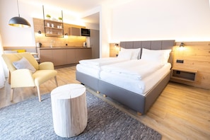 A modern hotel room with a large bed, a sofa, a round wooden stool, a kitchen area, and a wooden headboard. - Modern Alpine Apartment with Terrace (Hinterstoder)