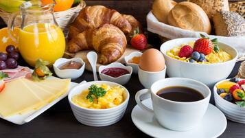 Une table dressée pour le petit-déjeuner avec des croissants, des œufs, des fruits, du fromage et une tasse de café.