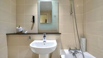 A bathroom with a sink, mirror, toilet paper, and a shower.