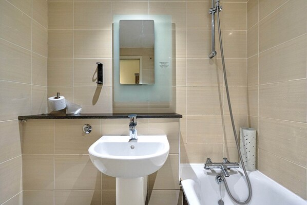 Une salle de bain équipée d’un lavabo, d’un miroir, de papier toilette et d’une douche.