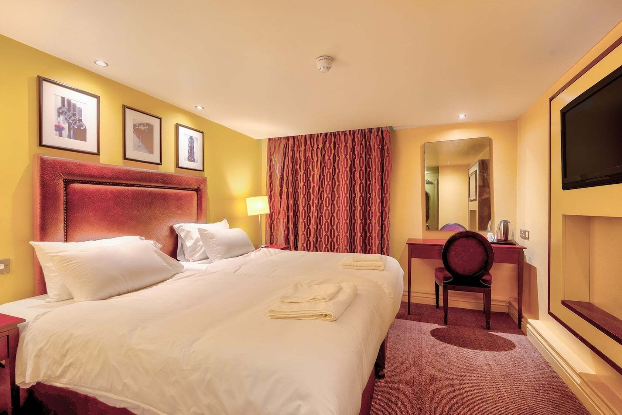 Habitación de hotel con cama, escritorio, silla, televisión y espejo.