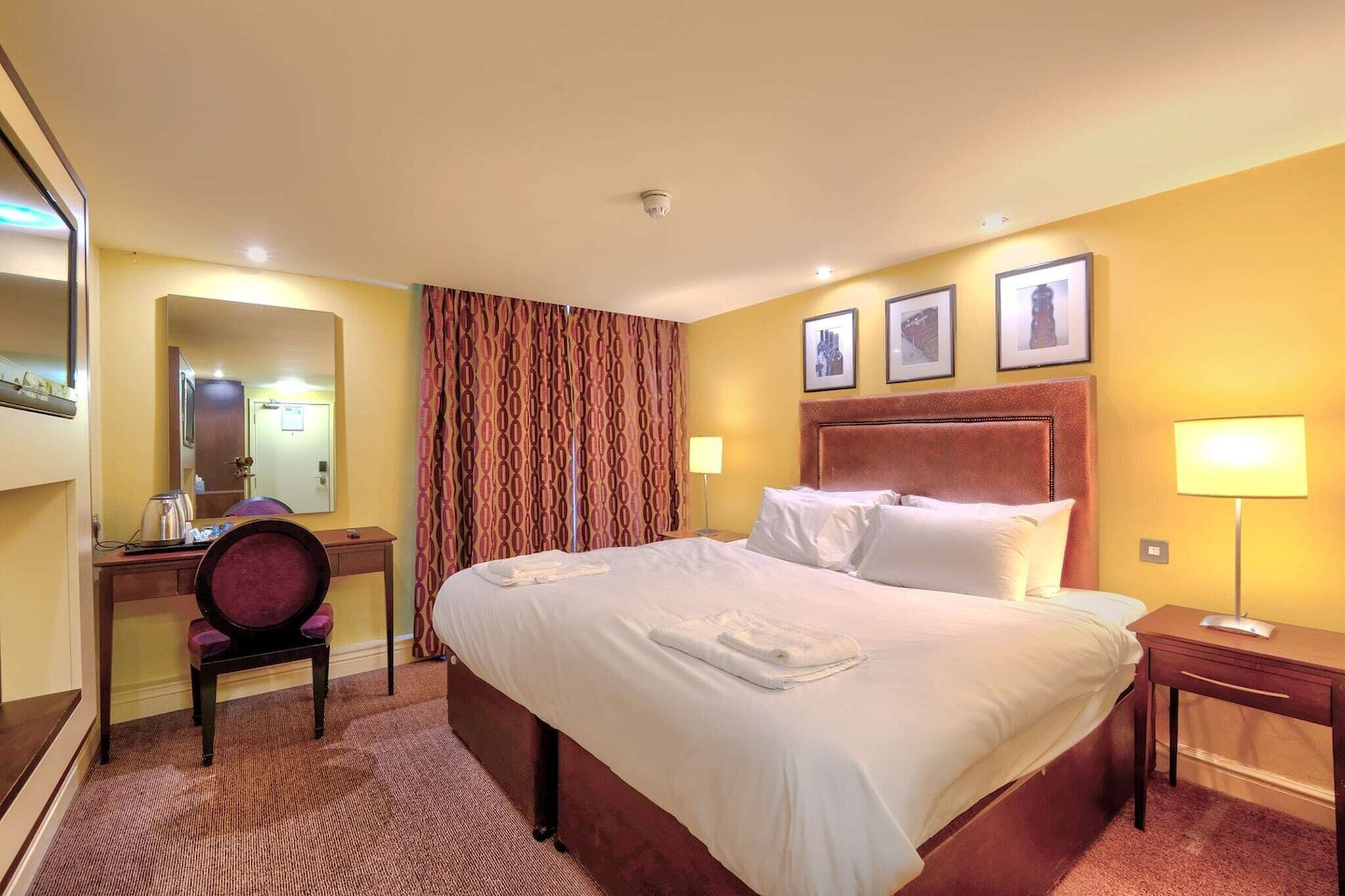 Ein Hotelzimmer mit Bett, Schreibtisch, Stuhl, Lampe und Spiegel.