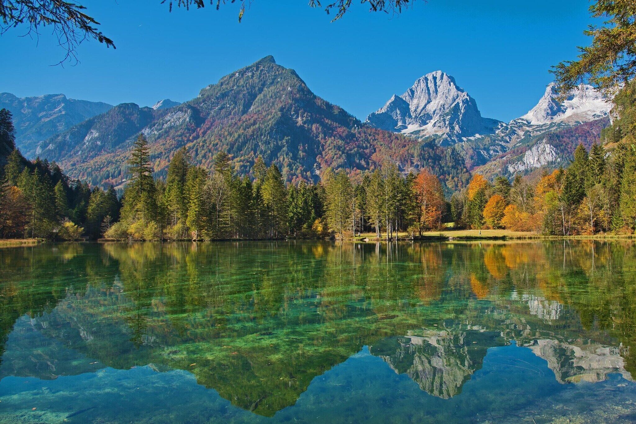 A clear lake reflecting mountains, surrounded by trees.