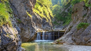 Een natuurlijke waterval in een rotsachtig klooflandschap, omgeven door weelderige begroeiing.